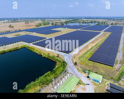 Vue surélevée d'une centrale solaire à grande échelle avec de vastes panneaux photovoltaïques située dans un paysage rural près d'un réservoir d'énergie propre. Banque D'Images