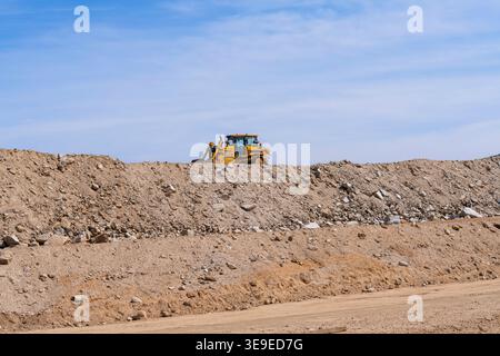 Le bulldozer fonctionne sur un chantier poussiéreux, déplaçant le sol et les roches sur un terrain accidenté sous ciel dégagé, mettant en valeur des machines lourdes et des terrains en développement Banque D'Images
