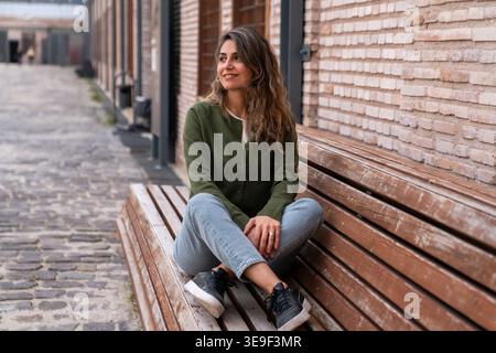 Jeune femme assise sur un banc en bois dans Urban Street Casual Lifestyle Portrait regardant loin. Banque D'Images