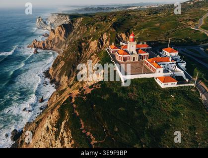 Vue aérienne du phare sur les falaises spectaculaires de l'océan avec des vagues s'écrasant le long de la côte accidentée au Portugal à l'heure dorée Banque D'Images
