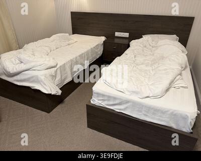 Lits jumeaux simples avec draps blancs et table de chevet en bois dans une chambre d'hôtel simple. Photo mobile Banque D'Images