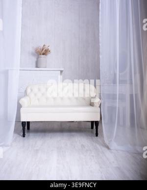 Intérieur confortable du salon décoré dans des tons blancs. Un canapé classique en cuir blanc de style chesterfield se trouve devant une cheminée ornée de séchés Banque D'Images