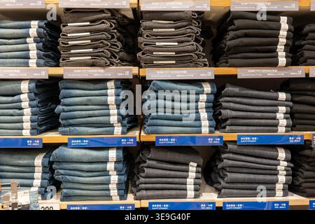 Hong Kong, Chine - 22 septembre 2025 : jeans en denim soigneusement pliés dans différentes tailles sur des étagères dans le magasin Uniqlo. Banque D'Images