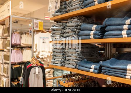 Hong Kong, Chine - 23 septembre 2025 : empilements organisés de pantalons en denim pliés dans différentes nuances bleues sur les étagères du magasin Uniqlo. Banque D'Images