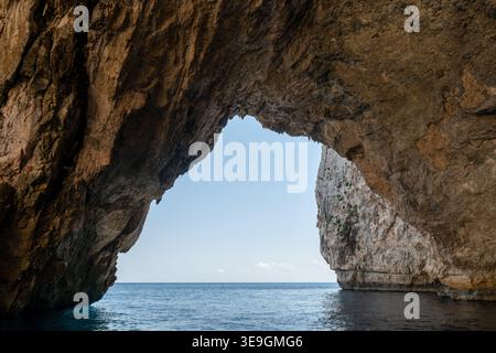 Vue depuis l'intérieur de la grotte marine Maltas Blue Grotto, encadrant l'horizon méditerranéen à travers une arche calcaire et une falaise à Qrendi. Banque D'Images