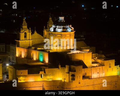 Vue nocturne de la cathédrale de Paul à Mdina, Malte, avec la façade baroque et le dôme illuminés au-dessus des murs de la vieille ville. Banque D'Images