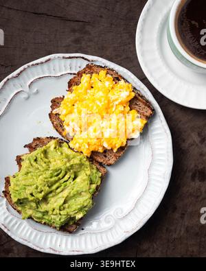 Délicieux pain grillé garni d'œufs brouillés et de guacamole. Scène de petit déjeuner confortable sur la table en bois rustique. Assiette blanche avec bord décoratif ajoute du charme. Da Banque D'Images