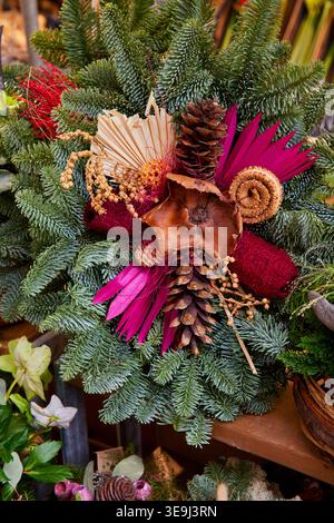 Couronne de Noël festive faite de branches de sapin vert décorées de pommes de pin, de feuilles séchées roses et d'ornements naturels. Banque D'Images