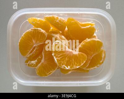 Segments d'orange mandarine pelés dans un récipient alimentaire en plastique transparent, vue de haut en bas, concept de collation saine ou de boîte à lunch. Banque D'Images