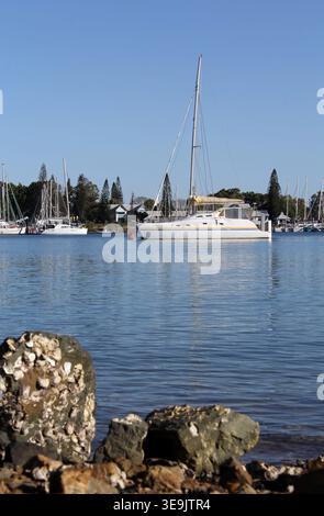 Bateau blanc amarré à la marina de Gladstone avec des rochers couverts de bernacle au premier plan et un ciel bleu clair dans le Queensland, en Australie Banque D'Images