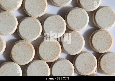 Macro-plan de haut en bas de plusieurs comprimés ronds et mouchetés de vitamine C disposés sur une surface blanche unie Banque D'Images