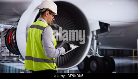 Le technicien portant un casque de sécurité examine minutieusement le moteur à réaction de l'avion pendant la vérification de maintenance Banque D'Images