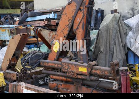 Machinerie lourde avec bras de grue hydraulique orange rouillé reposant au milieu de la ferraille à l'air abandonné et montrant une triste décomposition industrielle négligée dans un Banque D'Images