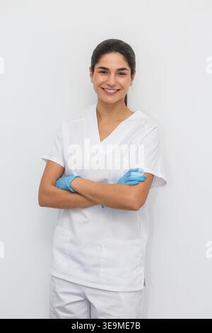 Un dentiste se tient dans une clinique dentaire, les bras croisés et sourit à la caméra. Le cadre est lumineux et clinique, mettant l'accent sur un environnement professionnel Banque D'Images