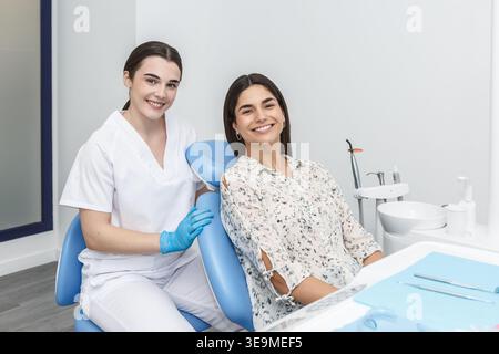 Une dentiste et sa patiente sourient assis dans une clinique dentaire. Le réglage montre l'équipement dentaire et les outils. Cette photo capture un CH dentaire de routine Banque D'Images
