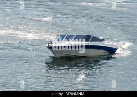 Bateau à moteur blanc et bleu naviguant sur l'eau pétillante lors d'Une journée d'été ensoleillée Banque D'Images