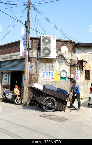 Un ouvrier local tirant un chariot lourd traditionnel rempli de déchets métalliques à travers les ruelles industrielles de Munlae-dong, Séoul. Banque D'Images