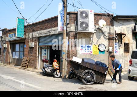 Un ouvrier local tirant un chariot lourd traditionnel rempli de déchets métalliques à travers les ruelles industrielles de Munlae-dong, Séoul. Banque D'Images