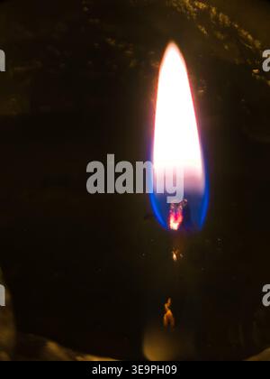 Gros plan d'une flamme de bougie éclatante avec des tons bleus et orange brûlant brillamment sur un fond de cire sombre et texturé. Symbolique de l'espoir, de la foi et de M. Banque D'Images