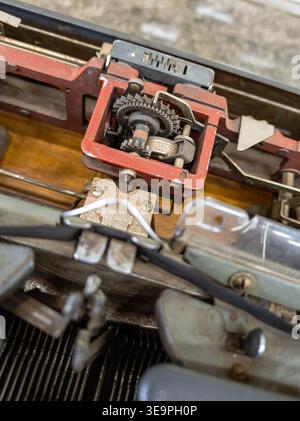 Vue détaillée du mécanisme interne complexe d'une machine à écrire vintage, présentant les engrenages exposés, les composants métalliques et la peinture rouge usée. Banque D'Images
