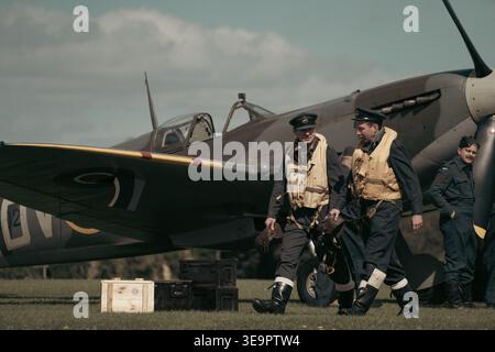 Deux pilotes de la RAF vêtus de gilets de sauvetage et de casquettes à pic marchent devant un Spitfire MkVc EE602 à l'aérodrome de Sywell, lors de la reconstitution de la bataille d'Angleterre. Banque D'Images