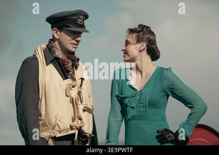Pilote de la RAF en gilet de sauvetage et casquette à pic discute avec une femme en robe verte à côté du Spitfire à l'aérodrome de Sywell Banque D'Images