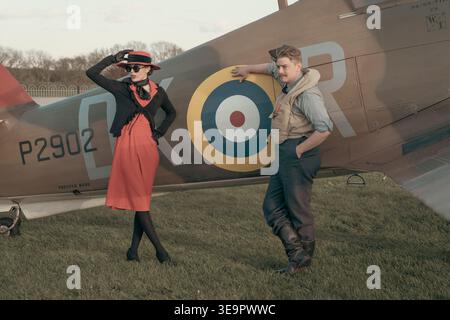 Femme en robe rouge et homme appuyé sur Hawker Hurricane Mk1 P2902 à l'aérodrome de Sywell, reconstitution de la seconde Guerre mondiale de la bataille d'Angleterre Banque D'Images