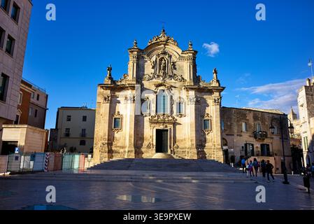 Les gens se promènent autour de l'église San Francesco à Matera, en Italie. Le bâtiment montre une architecture historique dans un ciel bleu clair. Banque D'Images