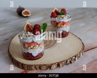Vue de face de deux desserts de chia en couches avec baies et granola sur tranche de bois naturel Banque D'Images