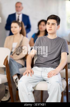 guy est assis dans la salle de classe contre le fond des autres étudiants et écoute Banque D'Images