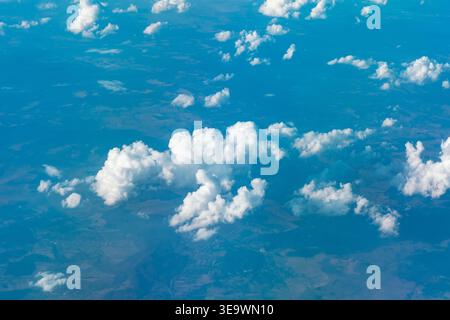 La vue aérienne époustouflante capture des nuages blancs pelucheux flottant au-dessus d'un patchwork de terres bleues en contrebas. La perspective d'en haut révèle la beauté de la Terre d'en haut Banque D'Images
