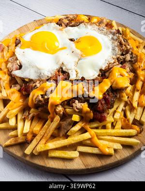 Frites dorées garnies de fromage fondu et de deux œufs ensoleillés. Les œufs fraîchement cuits brillent sur des frites savoureuses et copieux. Le fromage suinte de l'edg doré Banque D'Images
