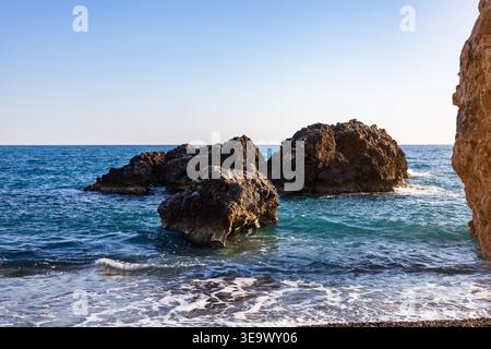Grands rochers accidentés dans l'eau bleue à la plage ensoleillée. Banque D'Images