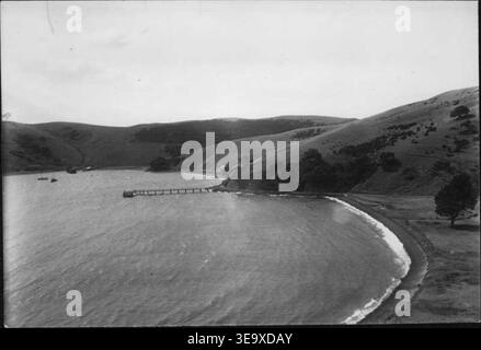 Henry Winkelmann (actif au début du XXe siècle) présente une vue panoramique de la Matiatia de l'île de Waiheke en 1928, mettant en valeur des plages en forme de croissant, une jetée s'étendant dans la mer, et divers bâtiments et bateaux au loin, y compris une épave. L'image d'archives offre un aperçu de l'environnement maritime et de la colonisation de Waiheke pendant cette période. Banque D'Images