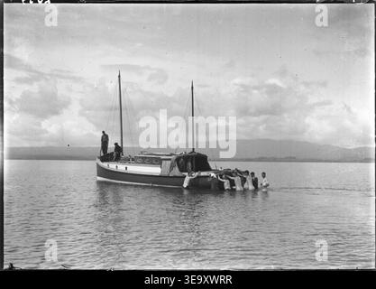 Cette photographie capture le bateau à moteur Uenuku qui s'échoue dans les appartements près de Katikati, en Nouvelle-Zélande, pendant la croisière Matareka. L'image, prise par Henry Winkelmann, montre plusieurs hommes dans l'eau qui tentent de libérer le navire, illustrant les conditions difficiles de la navigation au début du XXe siècle. Banque D'Images