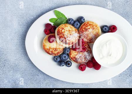 Petit déjeuner, gâteaux au fromage cottage, avec des baies fraîches et de la crème sure, vue de dessus, gros plan, pas de gens Banque D'Images
