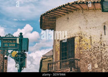 Une vue détaillée d’un bâtiment colonial altéré avec un balcon rustique en bois et des murs texturés, à côté d’un panneau municipal indiquant “Municipalidad de Banque D'Images