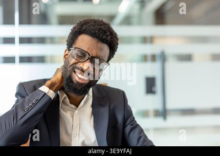Jeune homme éprouvant une gêne sévère au cou et une tension au travail, frottant ses muscles douloureux dans un cadre de bureau en raison d'une position assise prolongée et de tensions Banque D'Images