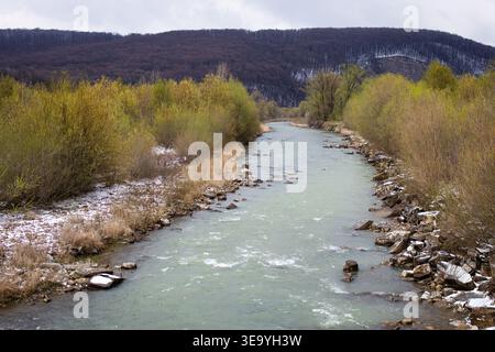 La rivière SWIFT traverse une vallée étroite avec des bancs rocheux et des bourgeons précoces sur des arbustes. Un ciel couvert et de faibles crêtes encadrent l'eau sinueuse comme source Banque D'Images