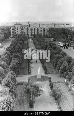 Sloviansk, 1956-1960, place de la Révolution d'octobre (aujourd'hui Soborna). Cette belle photographie d'archives historiques offre une vue surélevée saisissante d'une ruelle centrale méticuleusement aménagée. Deux bus interurbains classiques sont stationnés le long de la large route en arrière-plan, desservant la population locale. Des sculptures élégantes et des parterres de fleurs décoratifs ornent les allées symétriques. De grands bâtiments résidentiels bordent l'espace public verdoyant et luxuriant, soulignant l'urbanisme exceptionnel du Donbass paisible. Banque D'Images