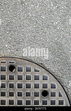 Couvercle de trou d'homme rond partiel avec asphalte texturé créant un fond d'espace de copie industriel urbain. Banque D'Images