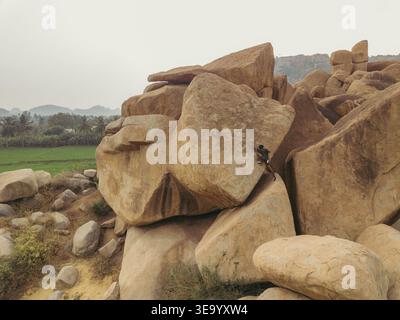 Vue aérienne de rochers altérés en cascade à travers le paysage, contrastant avec les champs verdoyants qui s'étendent vers l'horizon, Hampi, Karnataka Banque D'Images
