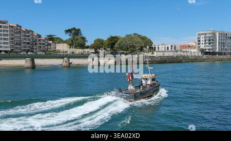 Les Sables-d’Olonne (centre-ouest de la France) : bateau de pêche sur le canal retournant au port, et vue sur les bâtiments du quartier chaume Banque D'Images