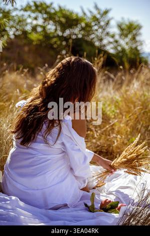 Dos d'une femme en chemise blanche assise dans l'herbe dorée Banque D'Images