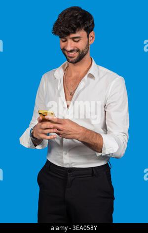 Homme souriant interagissant avec la technologie mobile, communiquant sur fond bleu Banque D'Images