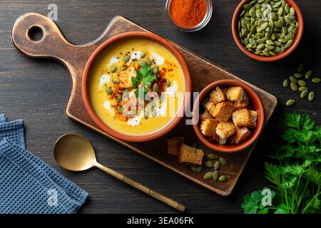 Délicieuse soupe à la crème de citrouille maison servie avec des croûtons croquants, des graines et de la crème dans un bol rustique sur un fond en bois, gros plan. Automne sain Banque D'Images