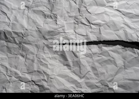 Texture spectaculaire de papier blanc froissé avec une déchirure diagonale montrant un espace sombre. Fond minimaliste grungy avec des ombres nettes et des bords de papier. Tor Banque D'Images