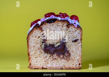 Gâteau sucré de Pâques tranché avec garniture au chocolat et cerises sur fond jaune. Coupe transversale d'un pain sucré avec du chocolat fondu à l'intérieur de la décoration Banque D'Images