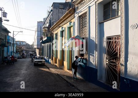 Une personne se promène le long d'une rue étroite bordée de bâtiments coloniaux colorés sous un soleil éclatant. Banque D'Images