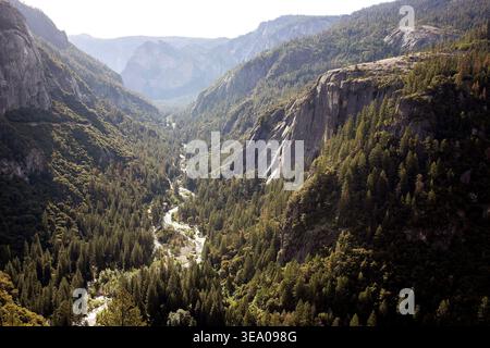 Une rivière sinueuse coule à travers une vallée verdoyante entourée de falaises rocheuses abruptes. Banque D'Images